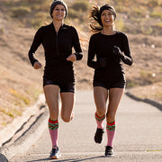 Two smiling runners wearing candy cane striped compression socks with red and green accents